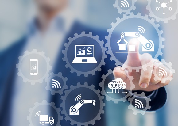 Smart factory and industry concept with connected production robots exchanging data with internet of things (IoT) and cloud computing technology, businessman touching interface with icons in gears