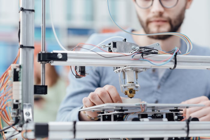 A man sits behind a 3D printer.