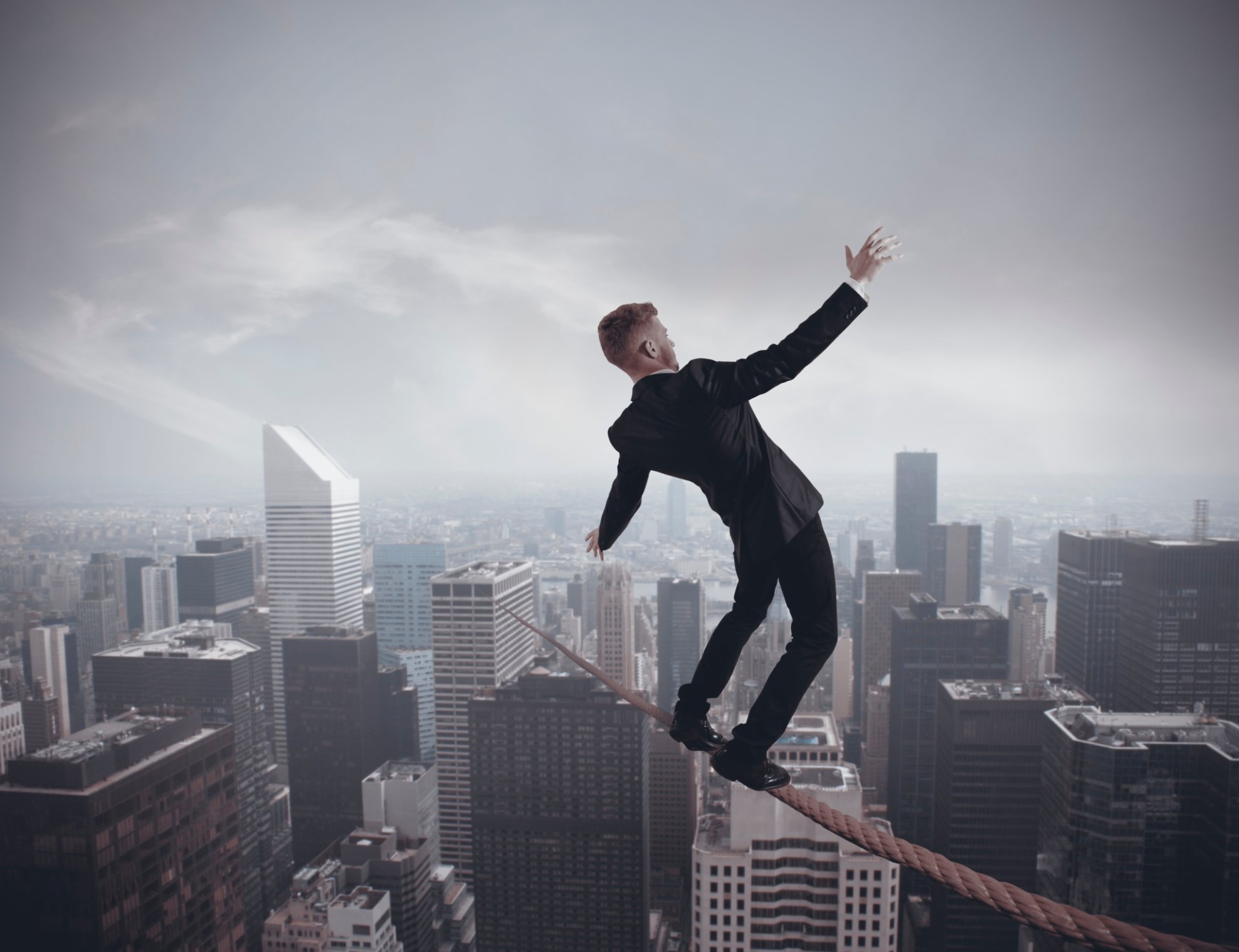 Businessman balancing on a tightrope over a computer-rendered cityscape.