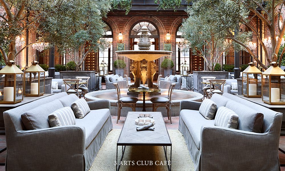 An atrium with foliage, gray couches, and other neutral-colored furniture surrounding a water fountain