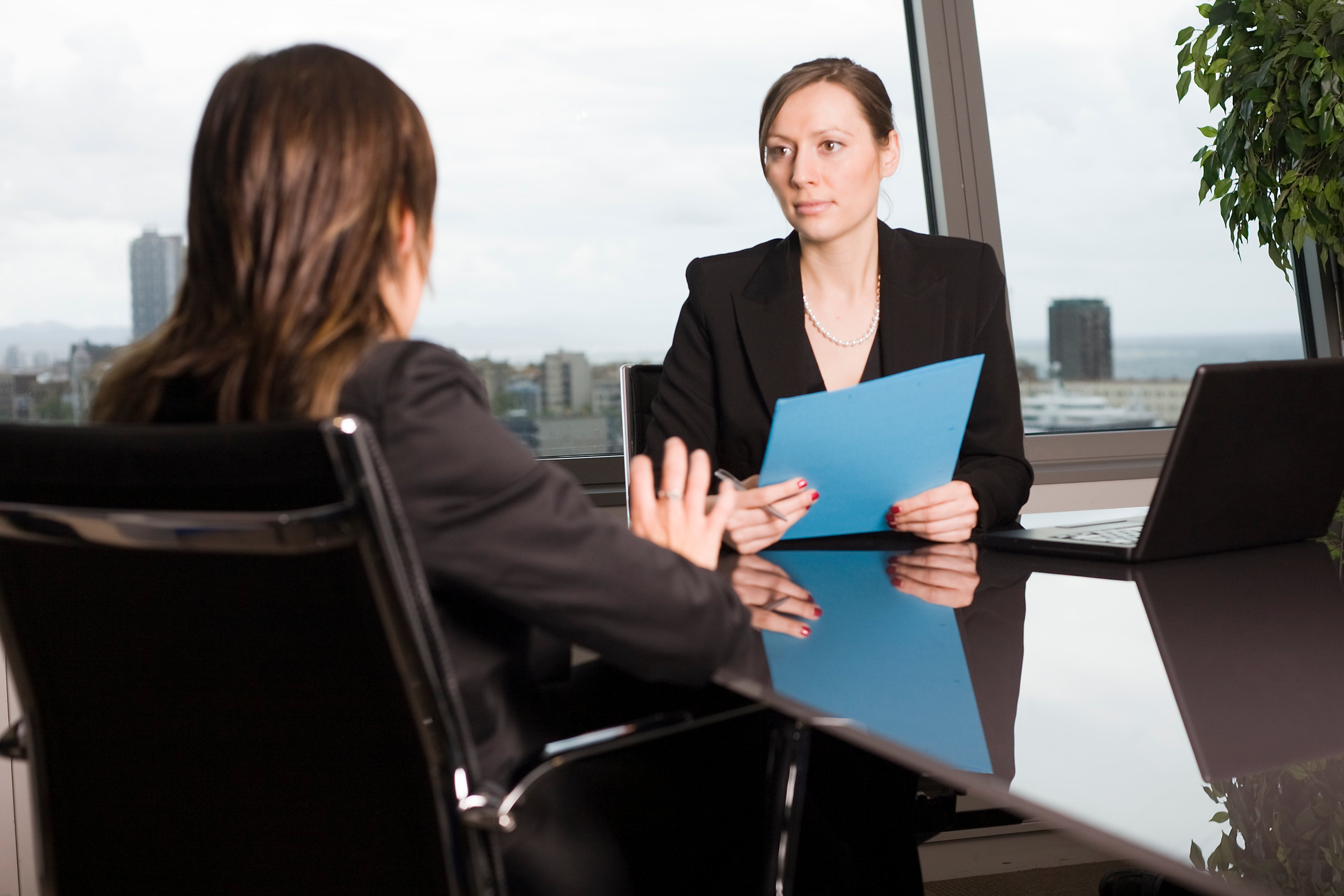 Two professionally dressed women seated at a conference table and talking to each other