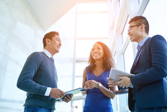 Two professionally dressed men and a professionally dressed woman smiling and having a conversation