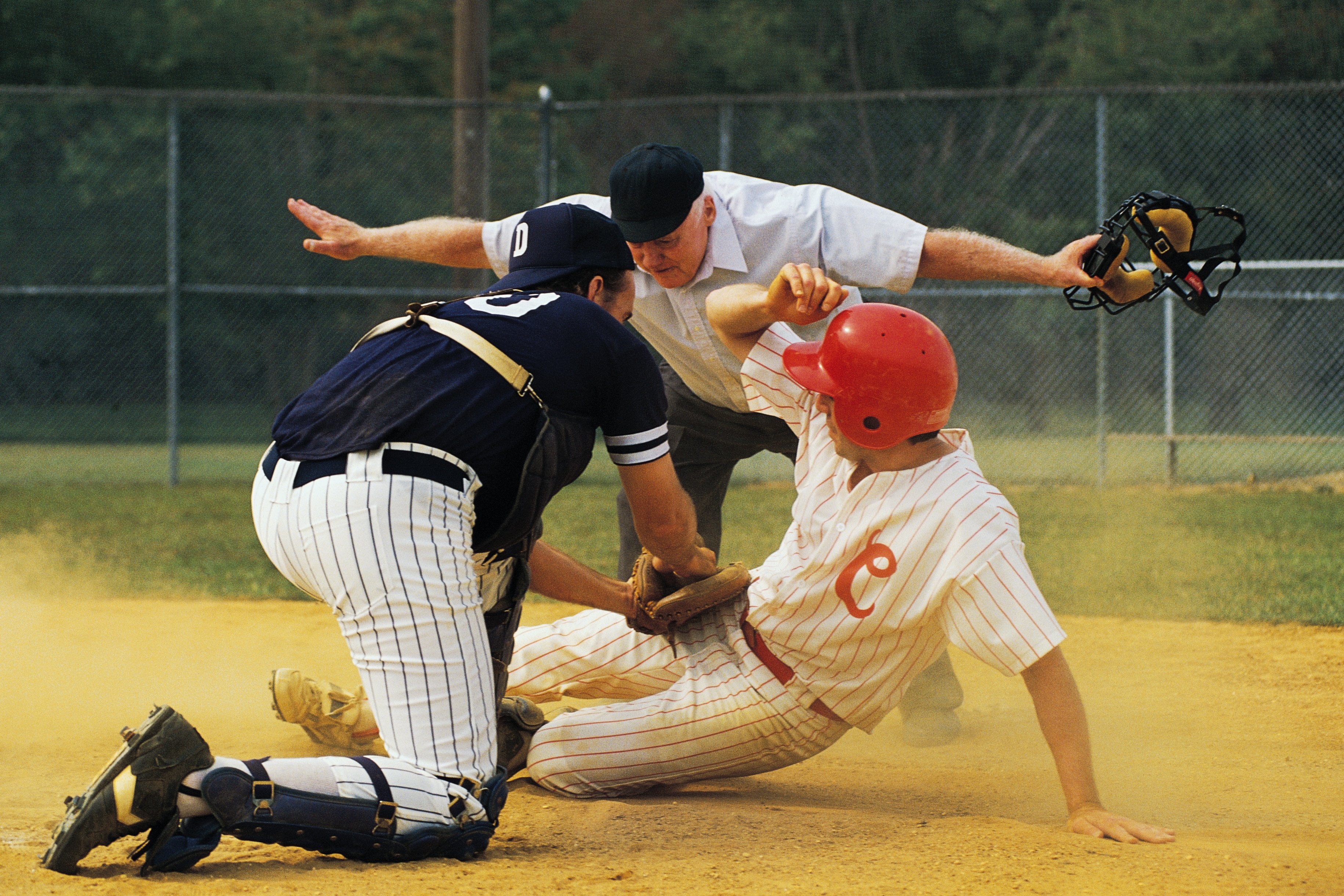 baseball player sliding into home base and umpire signaling with his arms that he's safe