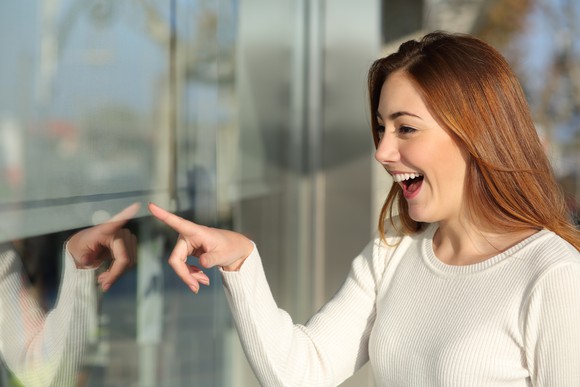 A smiling woman, pointing at a store window.