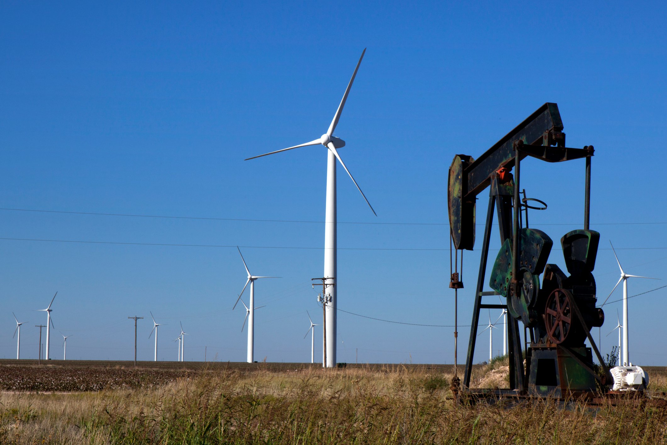 An oil rig and a wind turbine in a field.