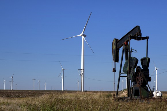 An oil rig and a wind turbine in a field.