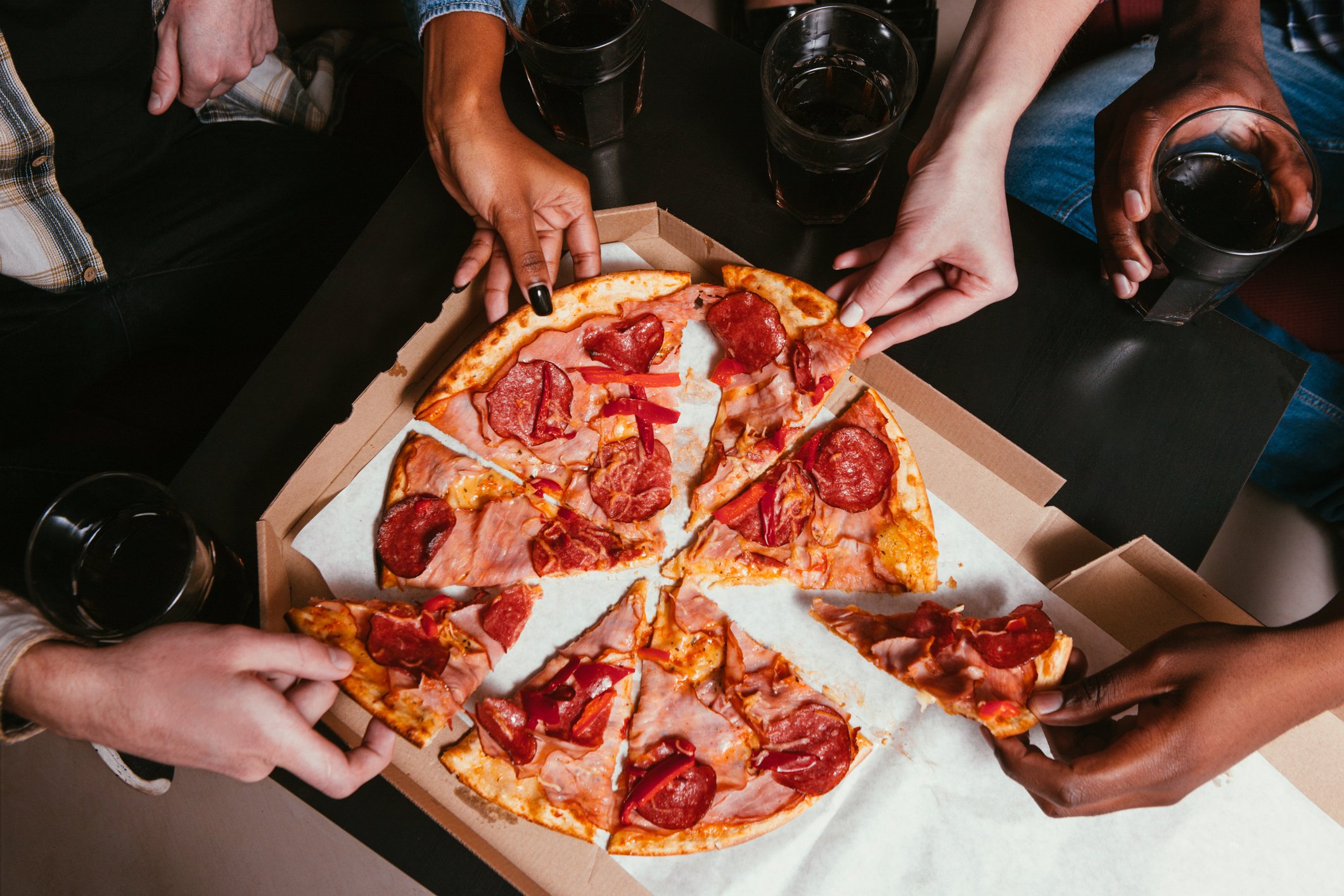 Four hands pulling slices of pizza from a pizza box