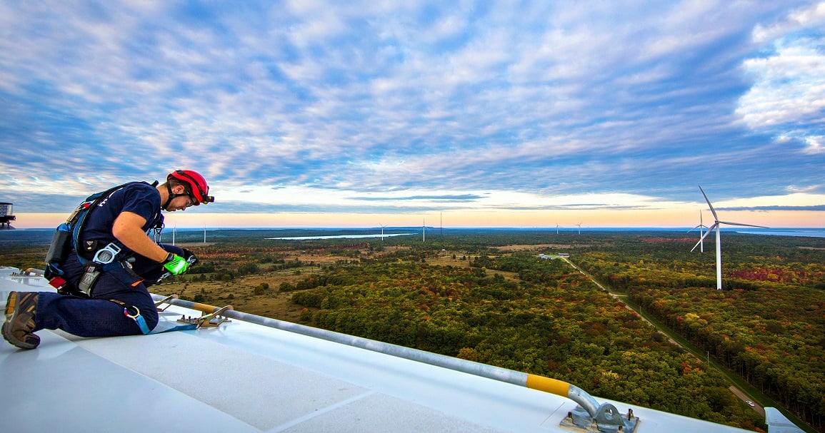 Worker on top of a wind turbine blade, looking across at other turbines in the background.