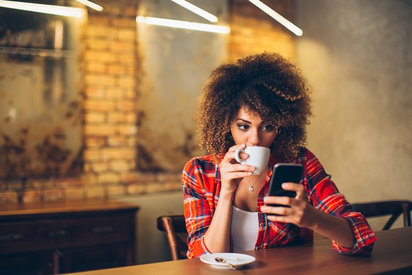 A woman using her smartphone while sipping on coffee