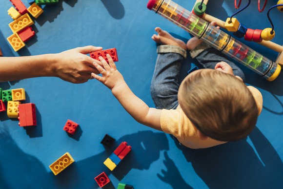 A young child is handed a connectiong block toy.