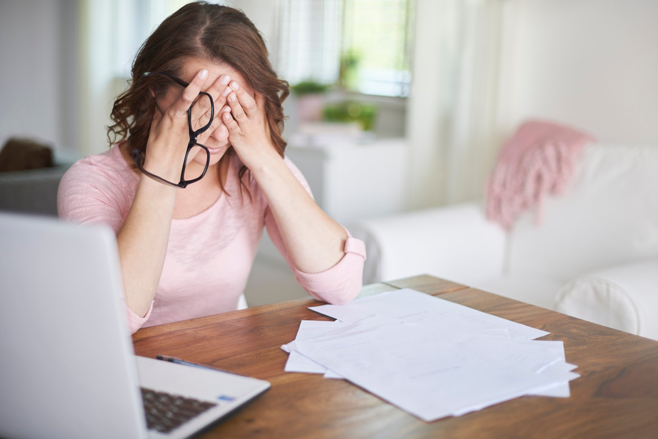 Woman at a laptop with papers in front of her, holding her head