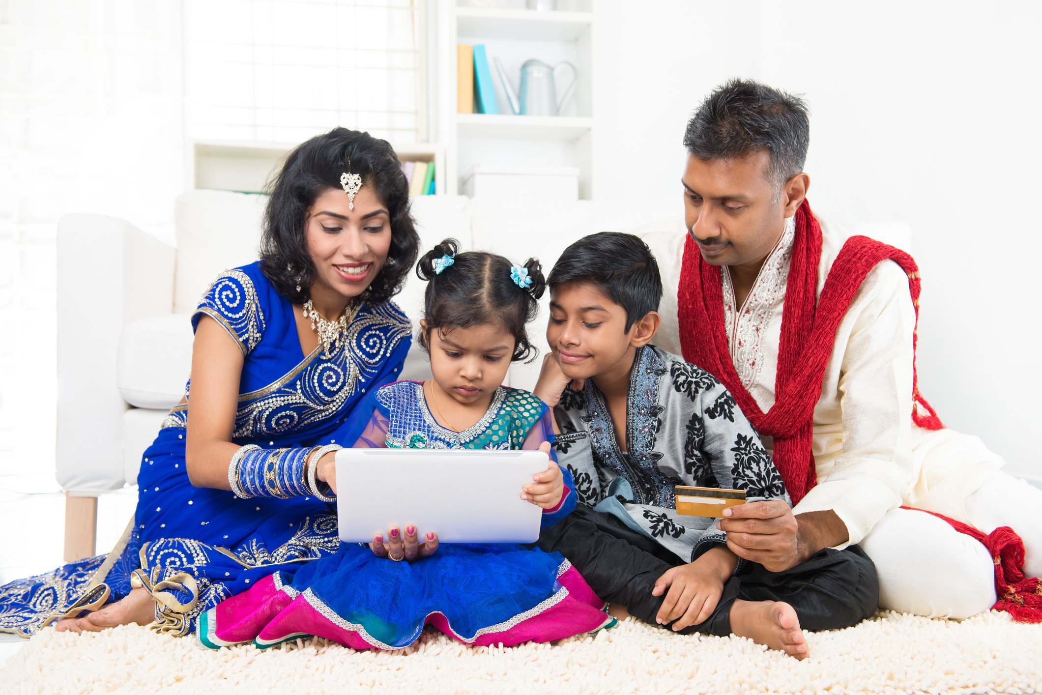 A young family in traditional Indian attire seated around a laptop making an online purchase. 