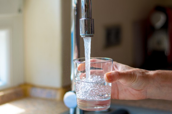 A hand filling a glass with water under a kitchen faucet.