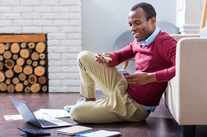Happy man purchasing an item with a credit card and mobile phone in his apartment.