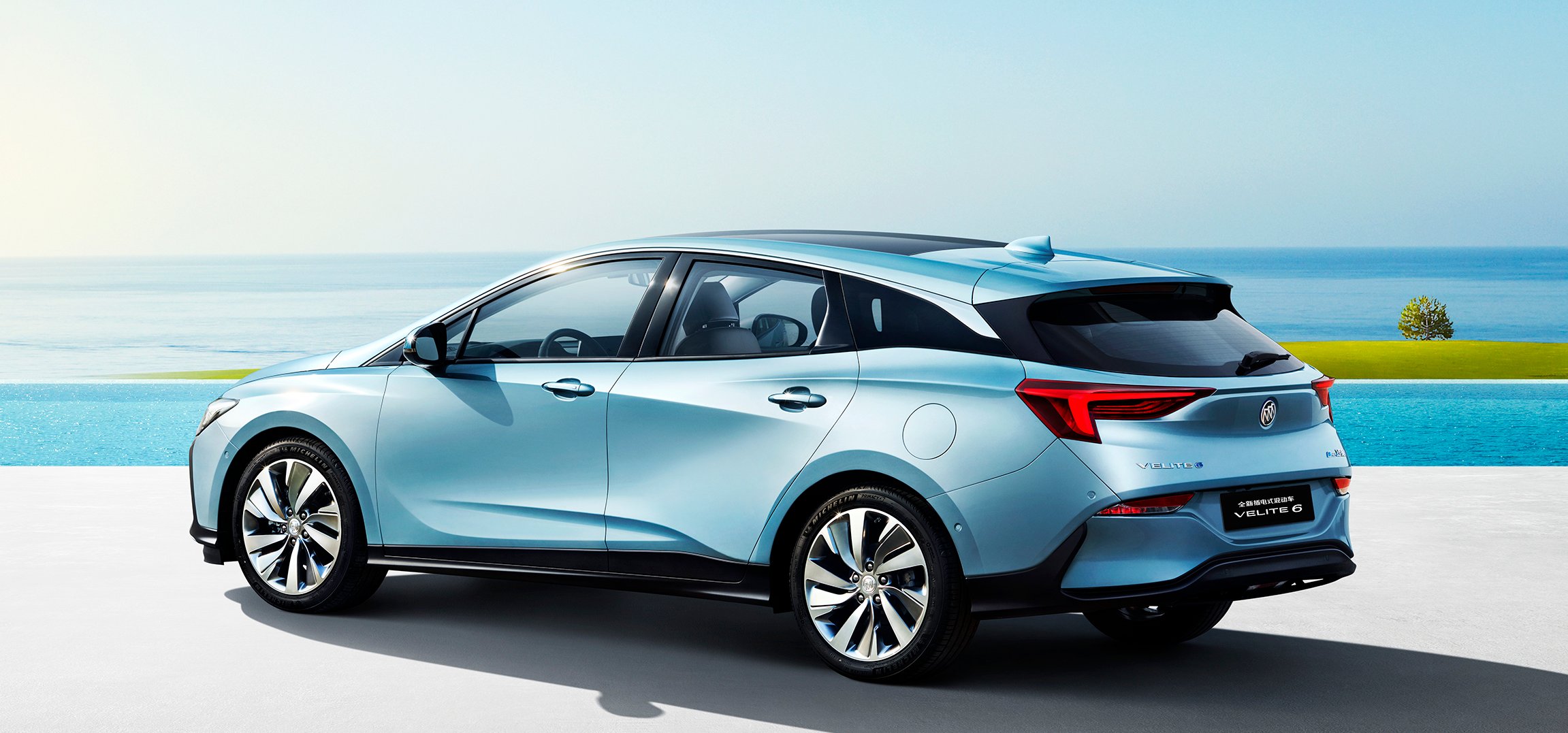 A rear three-quarter view of a blue Buick Velite 6, a station-wagon-like vehicle, on a beachfront.