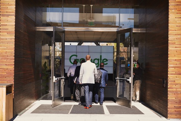 People in suits walking into Google's headquarters entrance.
