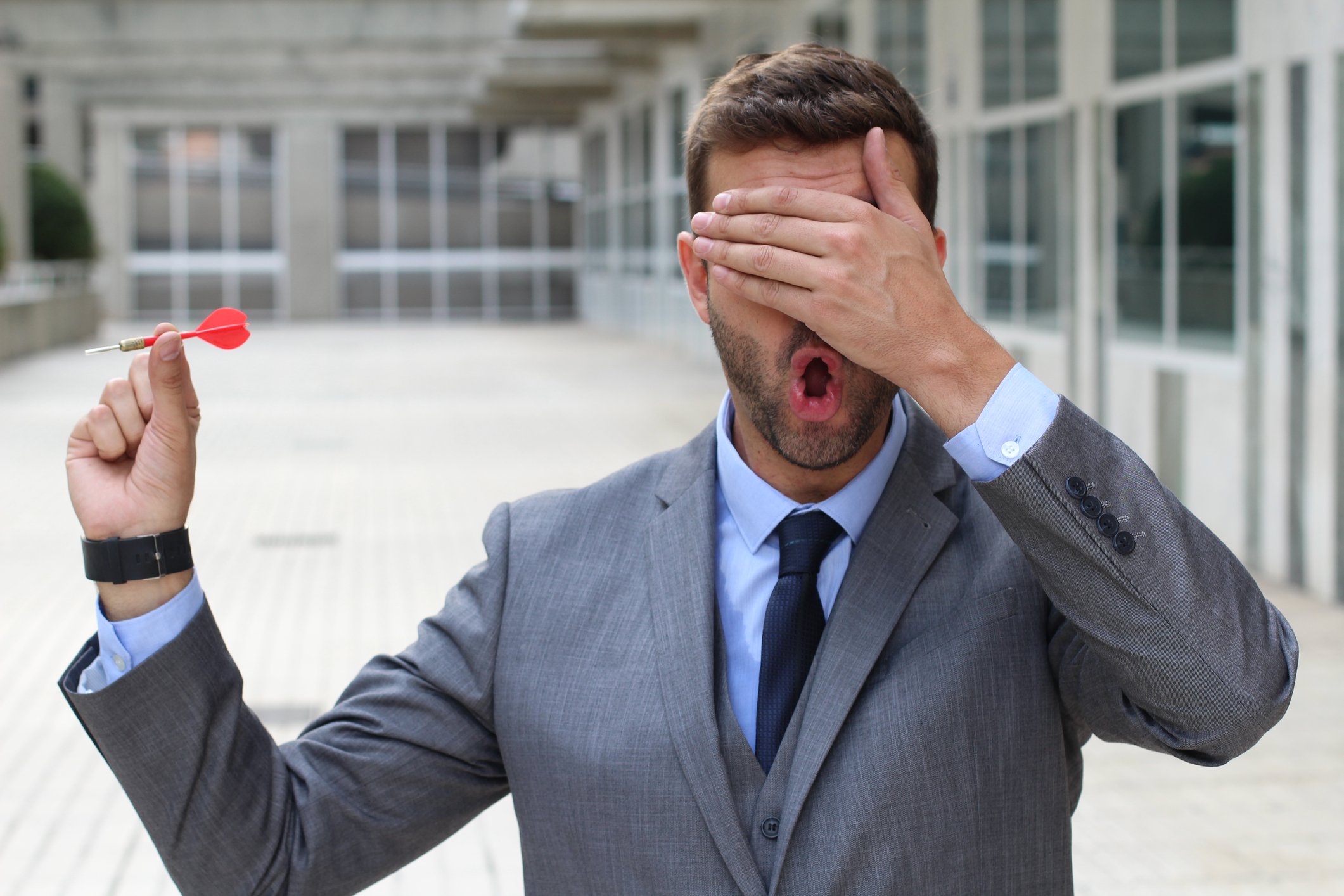 Businessman holding dart with hands over his eyes