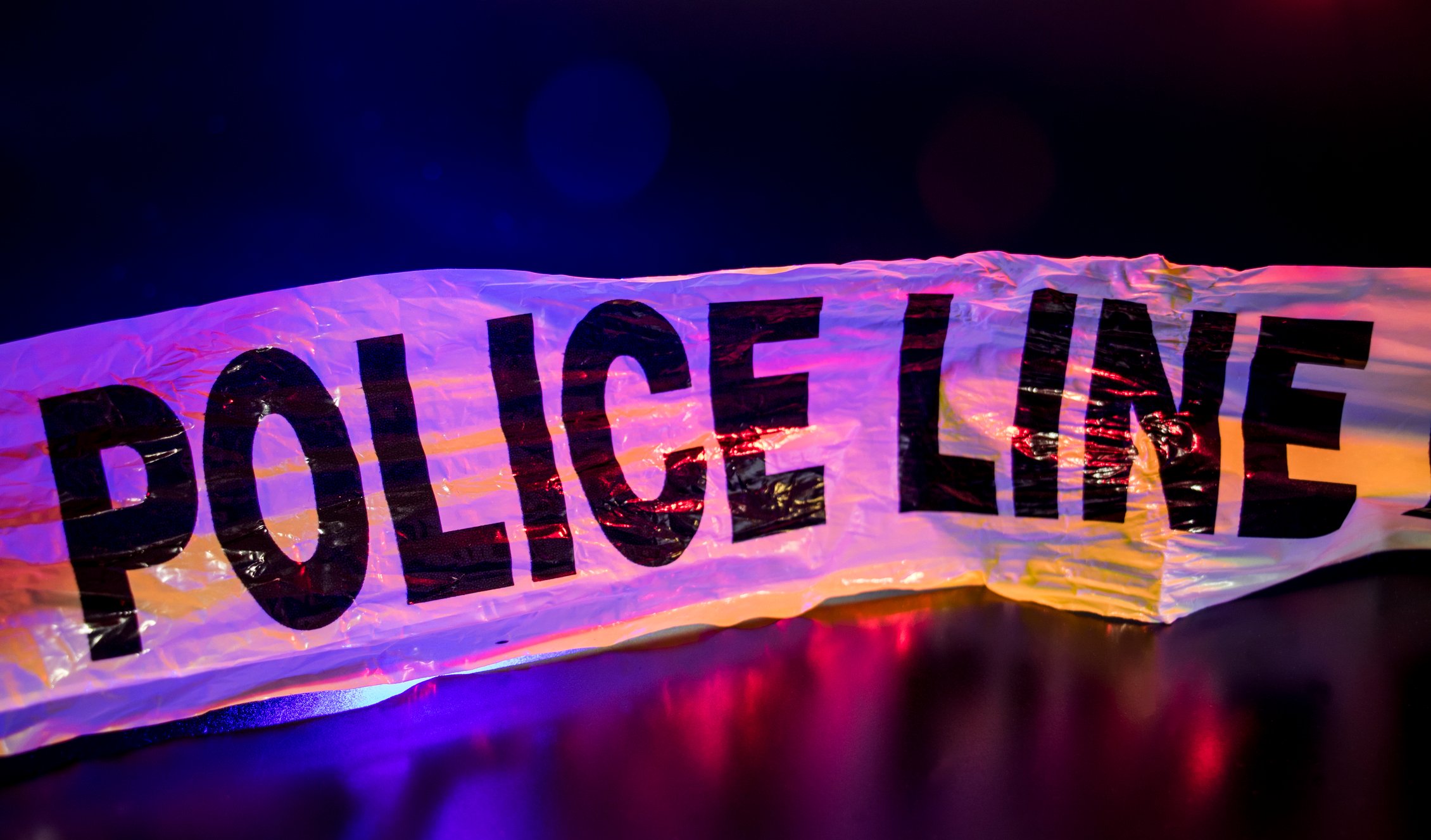 Crime tape reading "police line," backlit by blue and red lights.