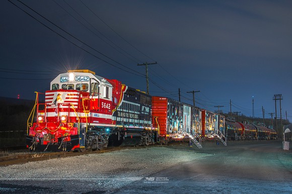 Train at night led by well-lit red locomotive engine.