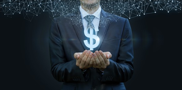 Man in business suit with his hands cupped beneath a glowing money sign that has dots hovering on top of it.