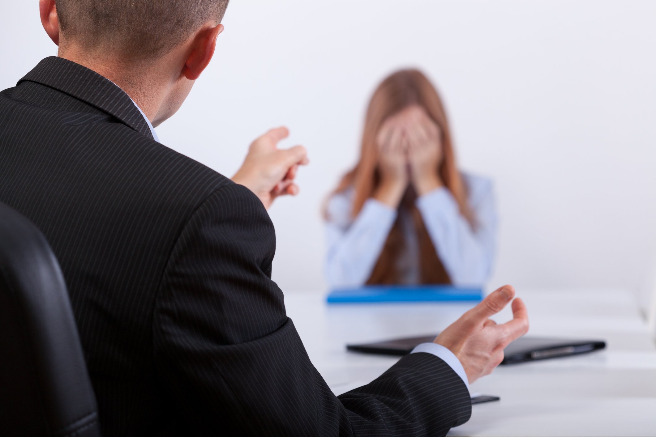 Woman covering her face while man in suit sitting across from her points a finger her way