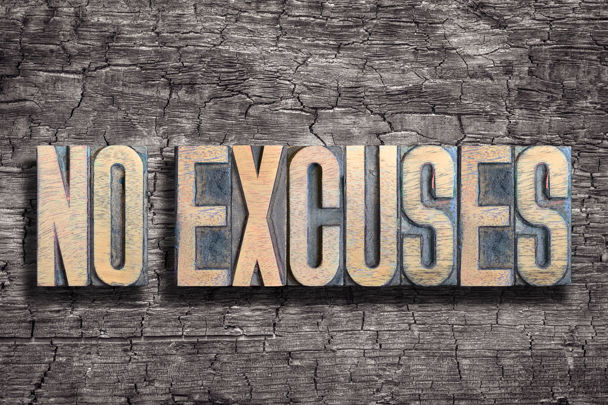 The words No Excuses in gold lettering on a wooden background.