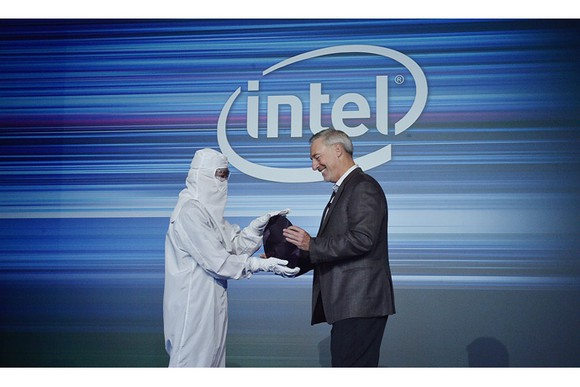 An Intel executive and an engineer holding a silicon wafer in front of a big Intel logo.
