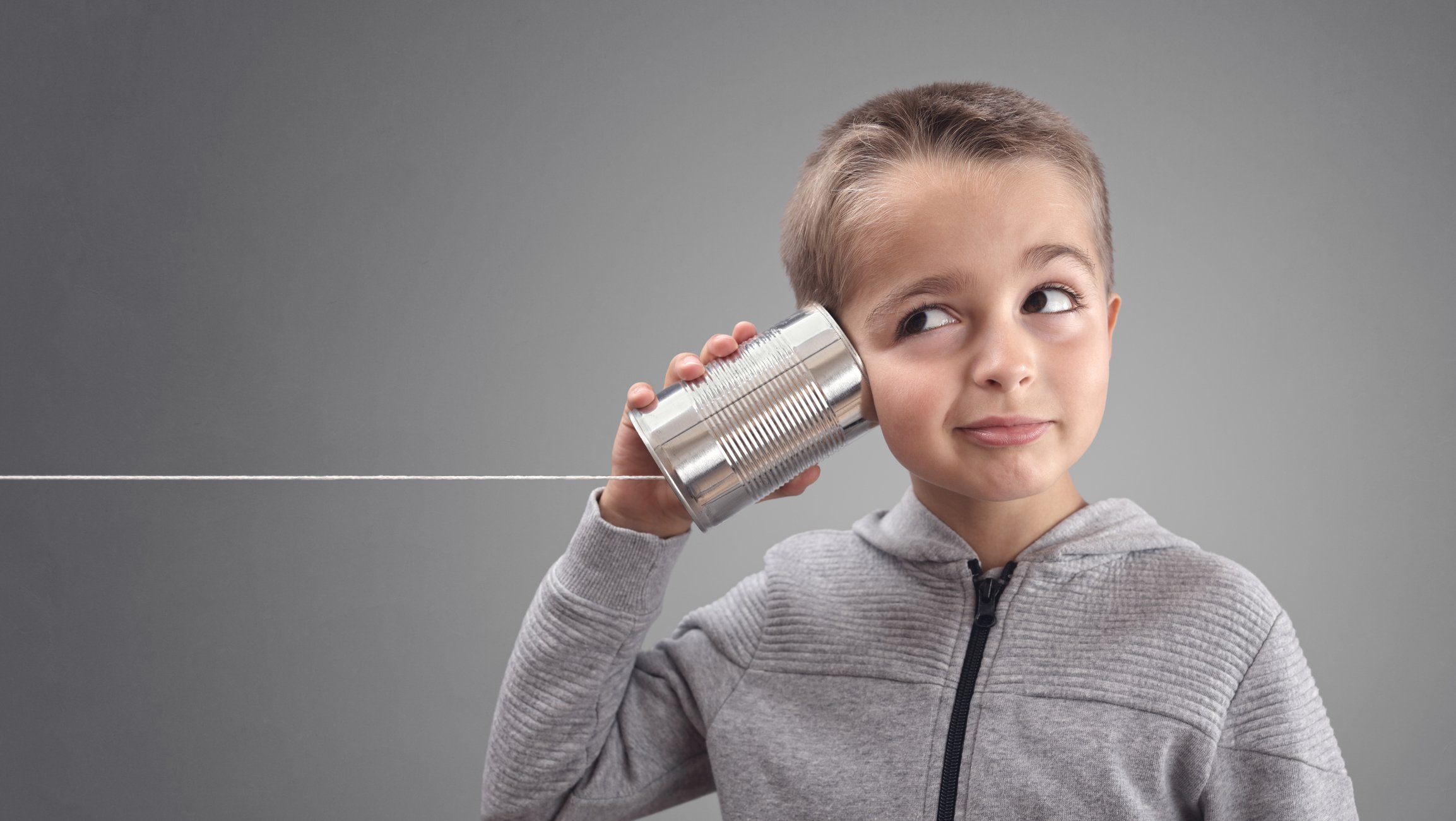 Child holding a can with a string attached to it up to his ear.