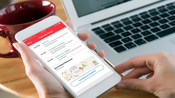 A person holds out their smartphone with information from the Grubhub app on it.