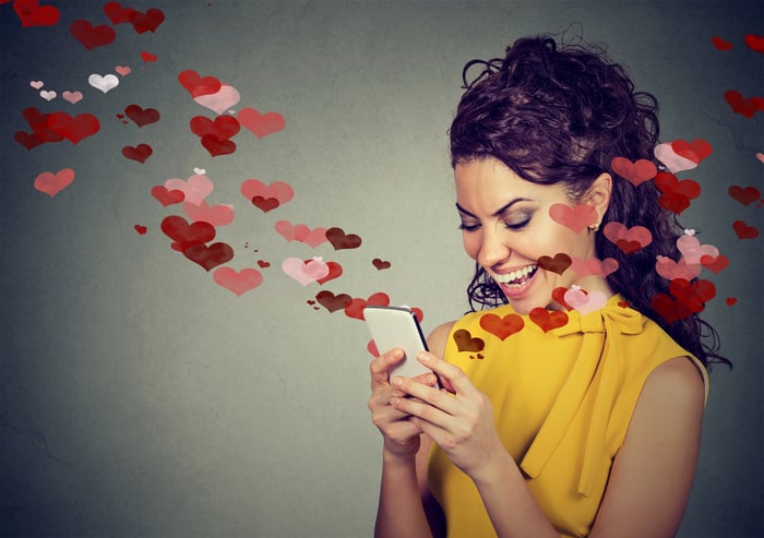 Woman smilling at her smartphone with hearts coming out of it