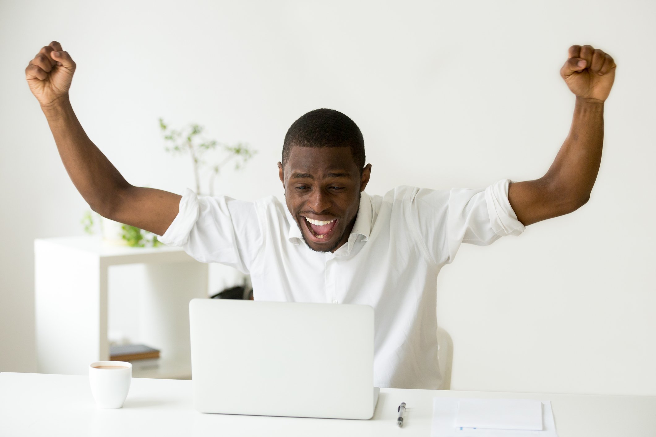 A man sitting at a computer raises his arms in triumph.
