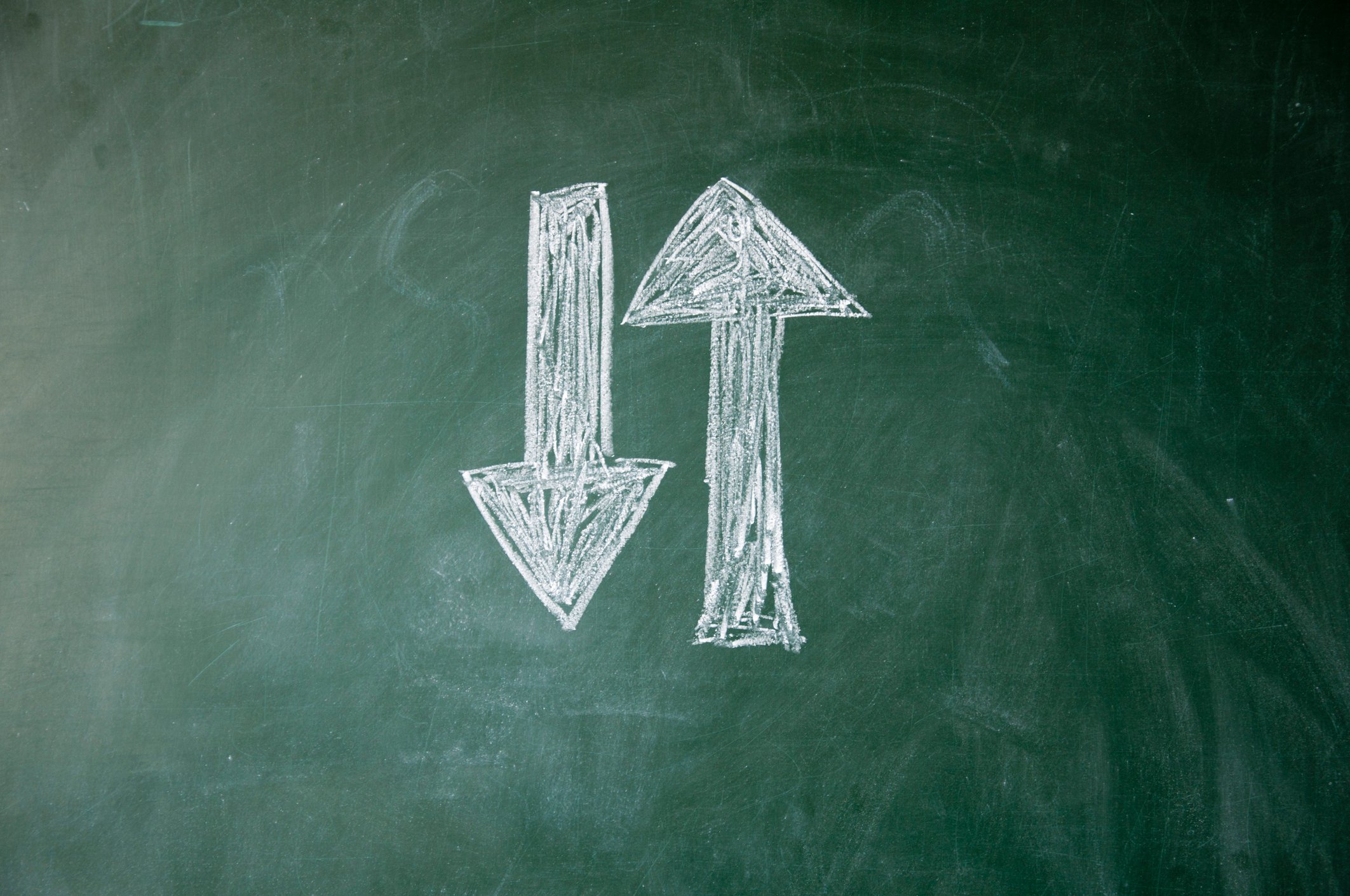 An up arrow next to a down arrow drawn on a chalk board.