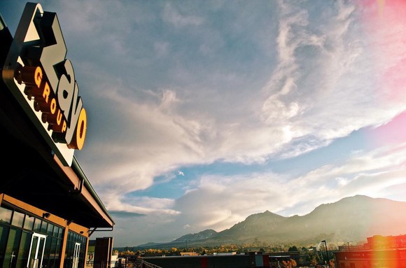 Building with Zayo Group sign with mountain landscape and partly-cloudy sky in background.