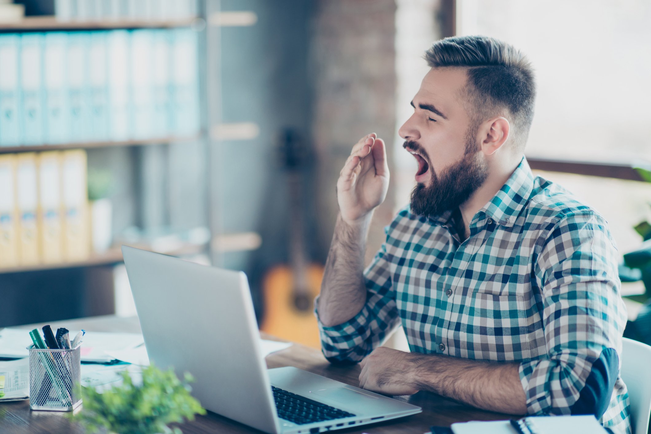 Man looking at laptop and yawning.