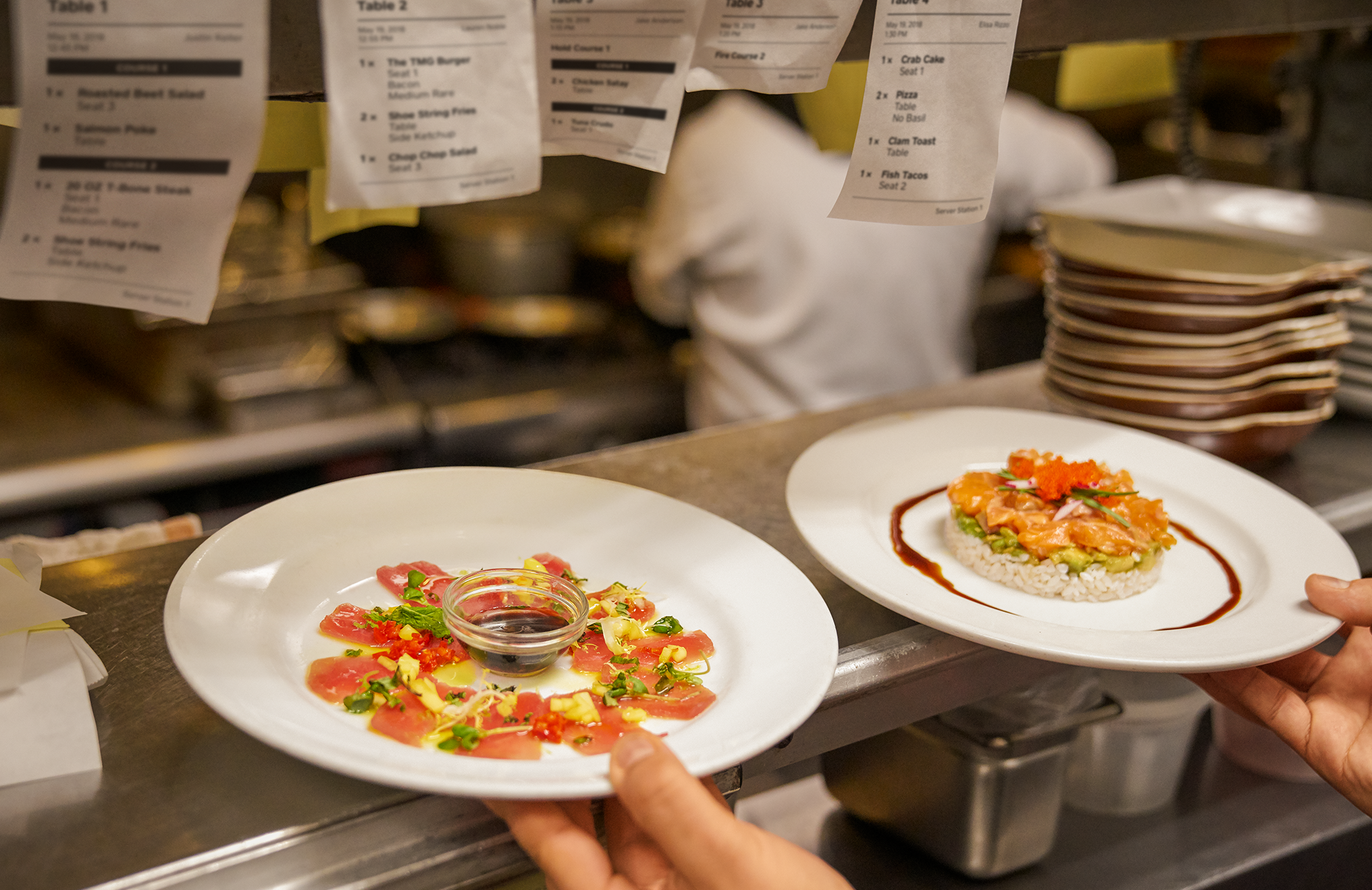A person picking up two plates from a restaurant kitchen counter.