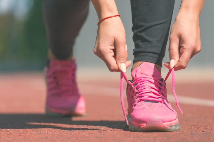 Female sport fitness runner tying her pink sneakers' shoelaces and getting ready for jogging outdoors on running track.