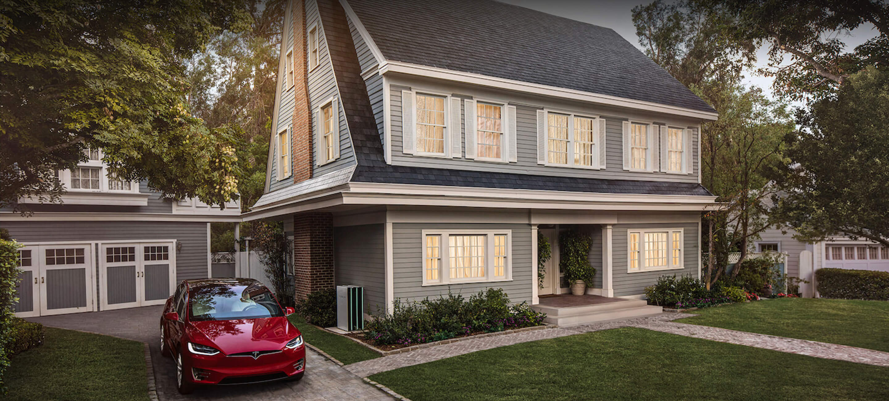 A gray house with a red Tesla Model 3 parked next to it in the driveway.