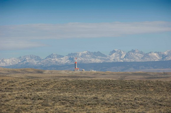 Land-based rig on semi-arid brush grass in front of mountain range.