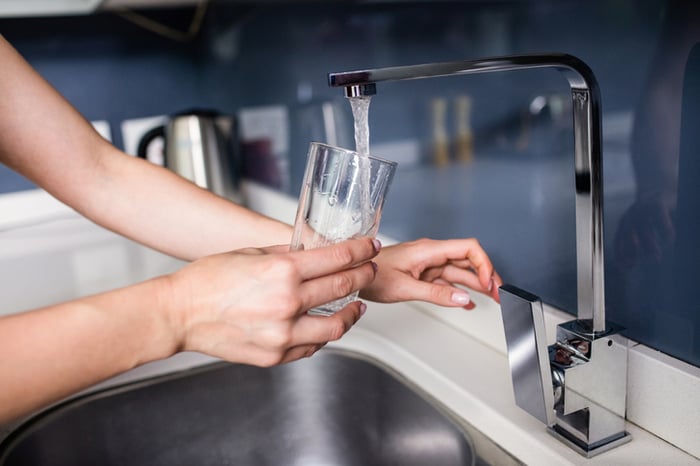 Person filling a glass under a water faucet.