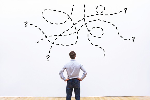 A man staring at a drawing of entangled dotted lines leading to question marks.