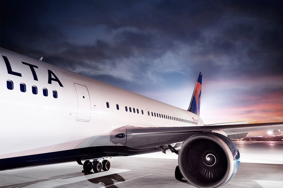 Delta aircraft as seen from left side, on a cloudy night near dusk on a white tarmac.