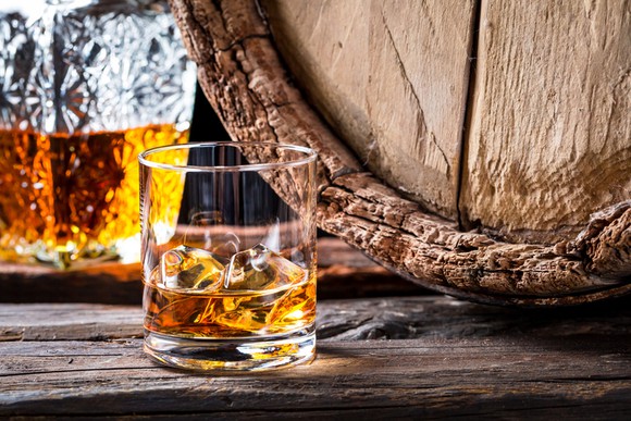 A glass of whiskey sitting next to a wooden barrel.