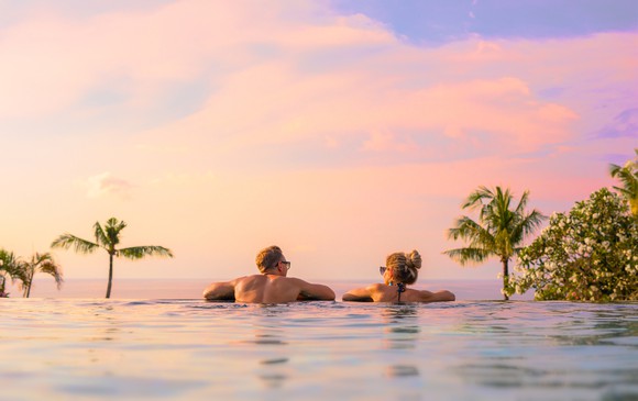 Two people leaning on edge of infinity pool with palm trees in the background