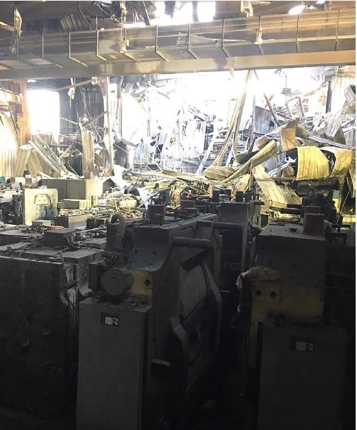 A photo of the factory floor after the fire, showing debris, tooling, and smoke damaged-walls. 