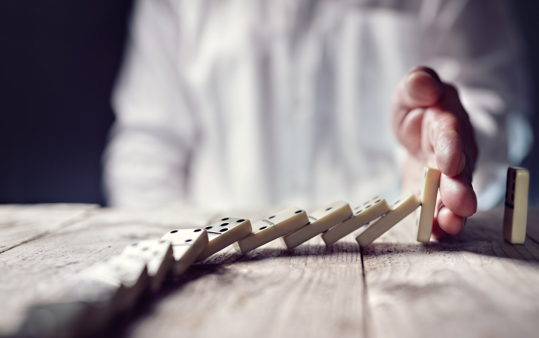 Man in white shirt uses his hand to stop the last domino from falling.