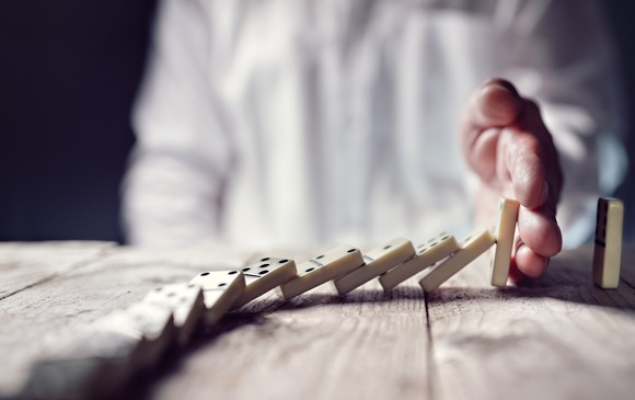 Man in white shirt uses his hand to stop the last domino from falling.