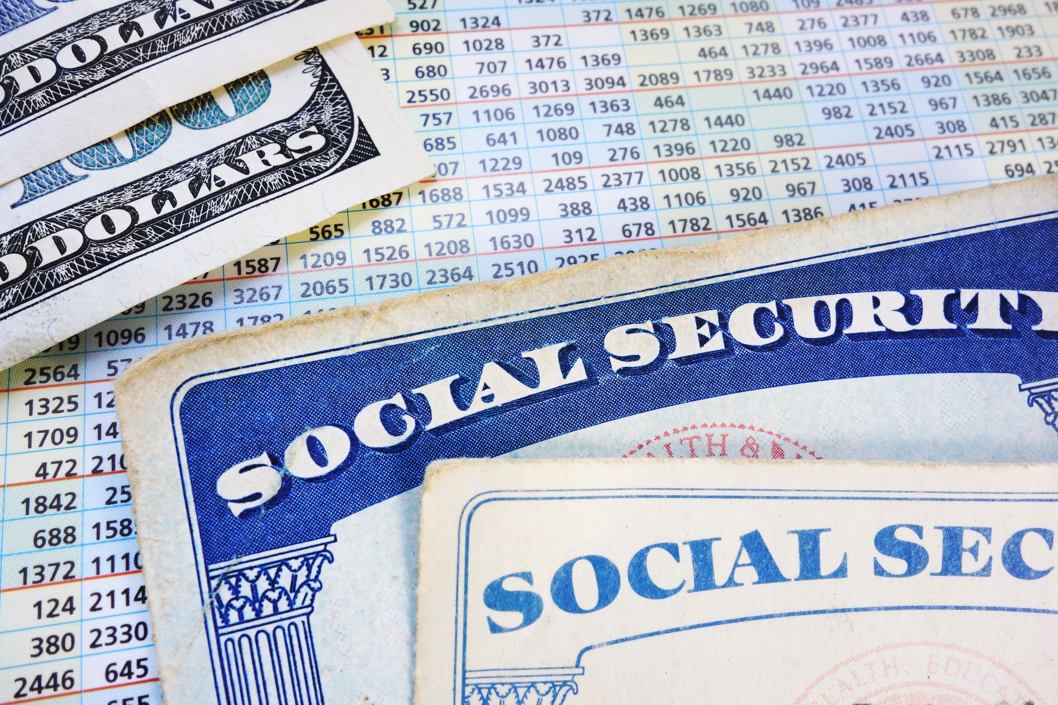 Social Security cards lying atop a benefits calculation card, and next to a small pile of hundred dollar bills. 