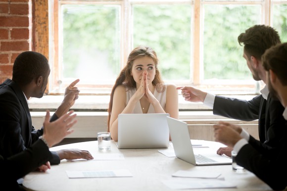 Four people sit around a conference table and two point at one woman.