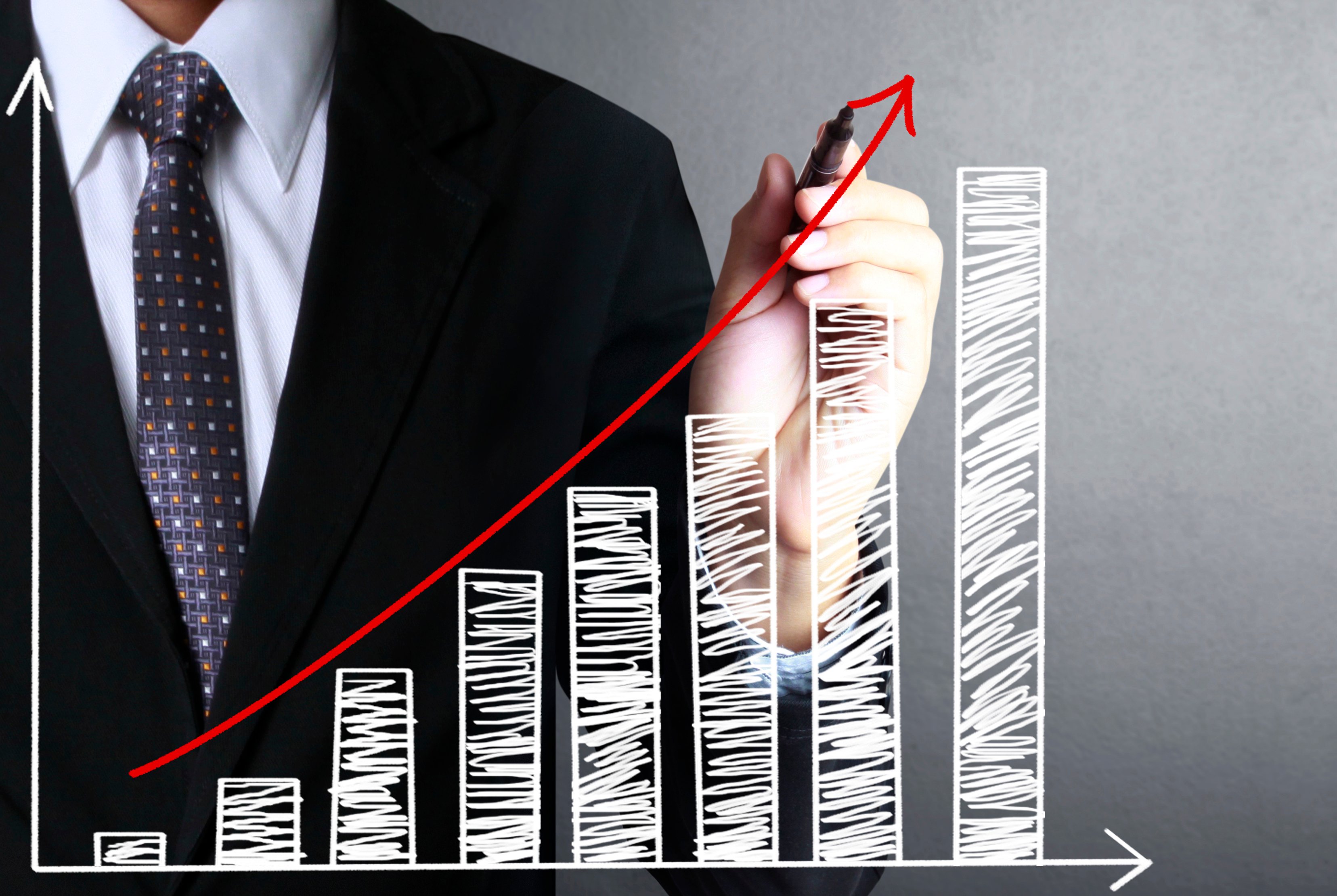 A person in a suit drawing a red line to show the upward trend of a white bar chart.
