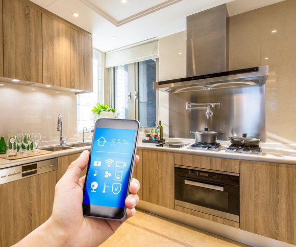 A person controlling appliances and lights in a kitchen using a smartphone.
